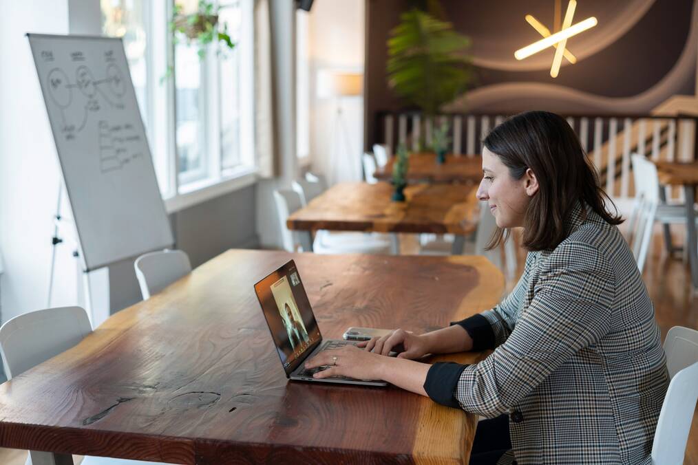 A woman dressed professionally makes a video call on her laptop.
