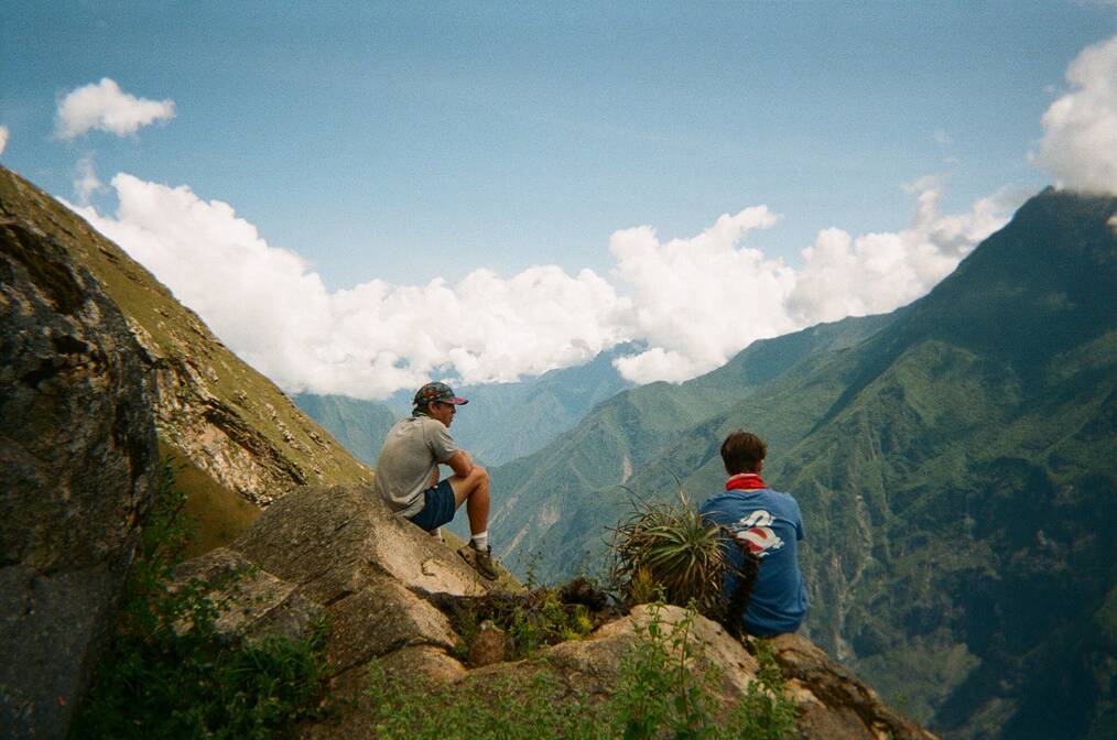 2 Travelers sitting on a mountain together looking at the view