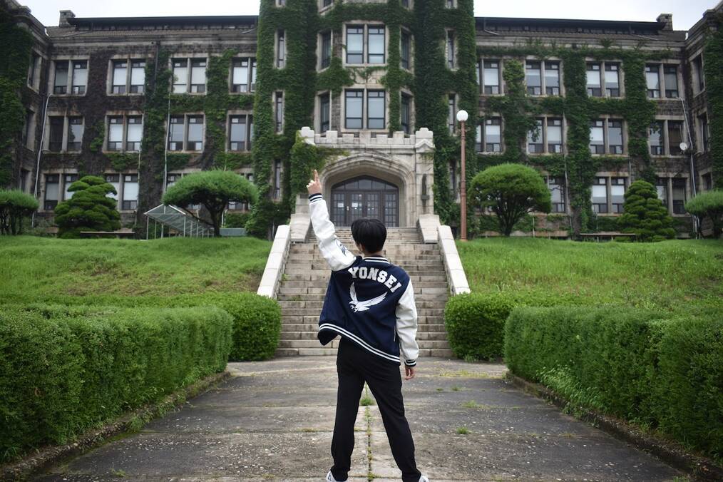 A student standing in front of their university with their hand raised in the air