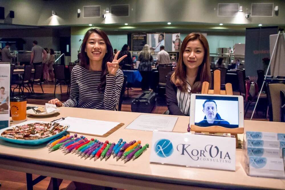 Two recruiters pose at a table with pens on it.
