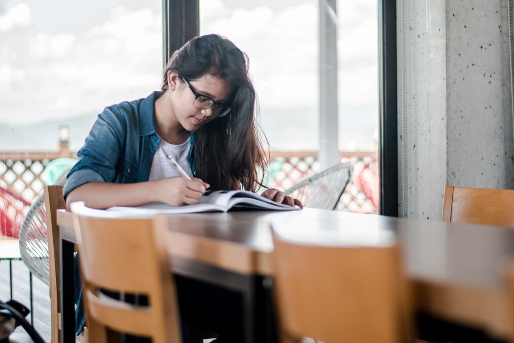 Photo by Kyle Gregory Devaras on Unsplash A woman sitting at a desk writes in a notebook.