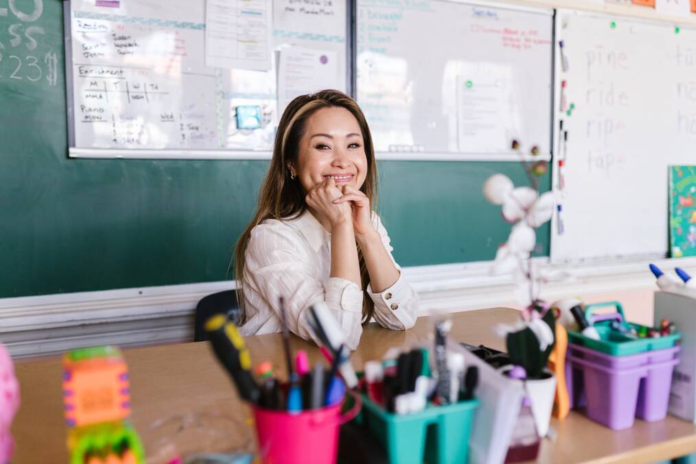 A teacher sits at her desk smiling.