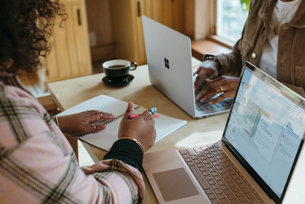 Photo by Surface on Unsplash Two women work on laptops on a table.