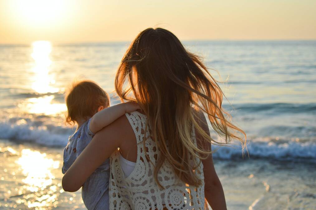 Woman holds a baby on the beach.