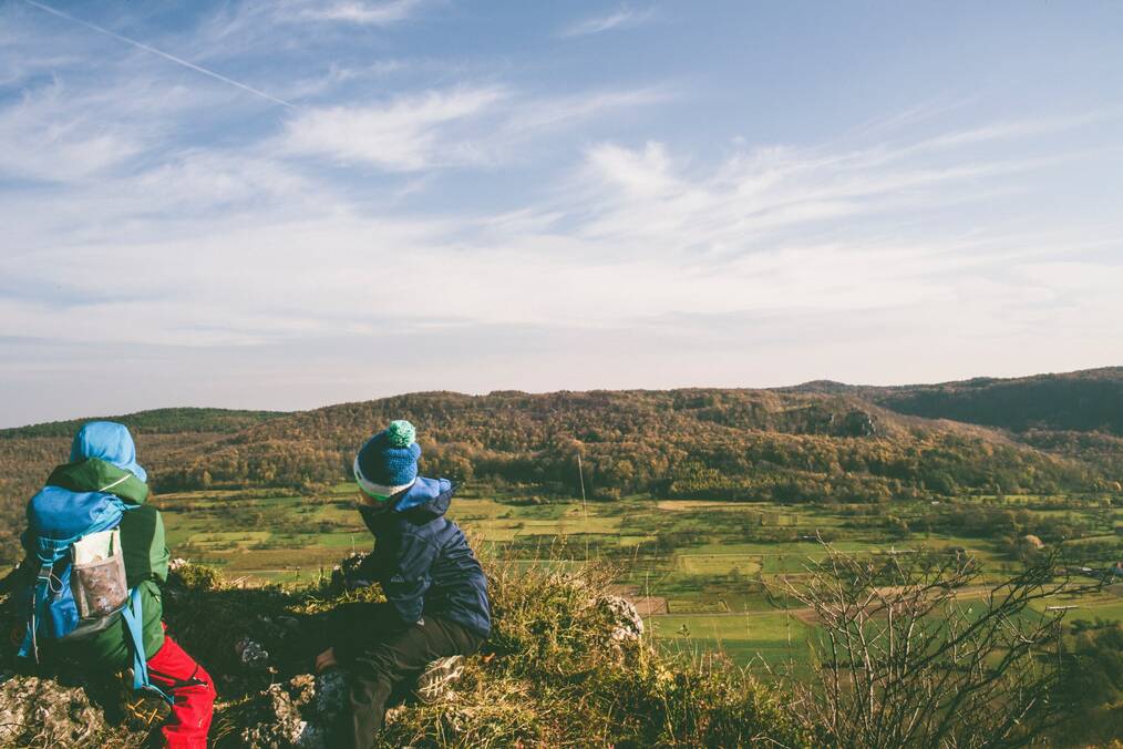 Two kids sit on a hill overlooking a green valley.