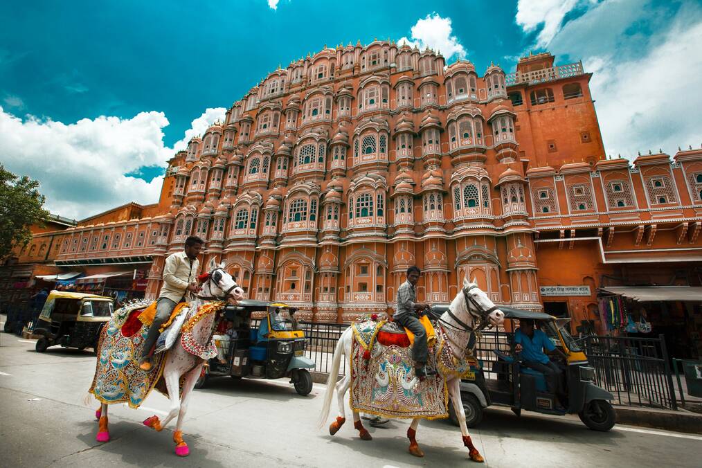 Two men ride horses with decorative saddles in the street in India.