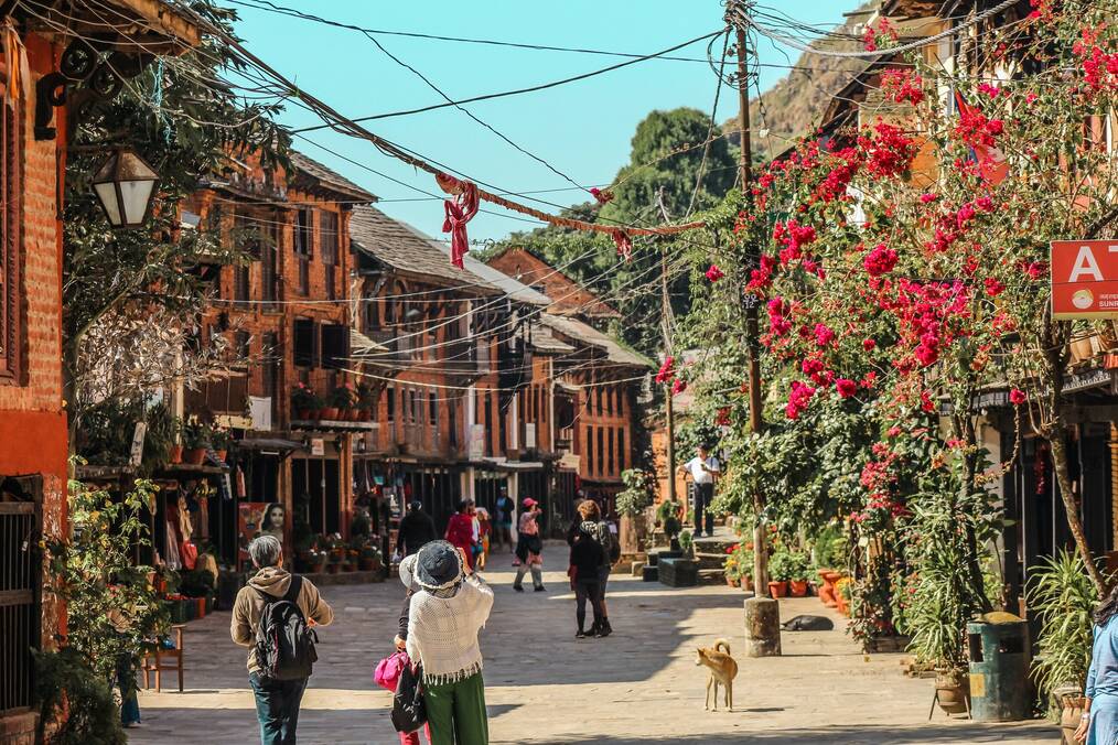 People walk down a street lined with vegetation and buildings in Bandipur, Nepal.