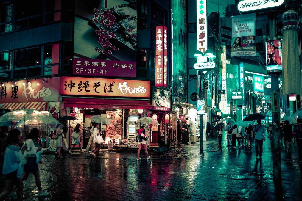 People walk with umbrellas under neon signs in Tokyo.