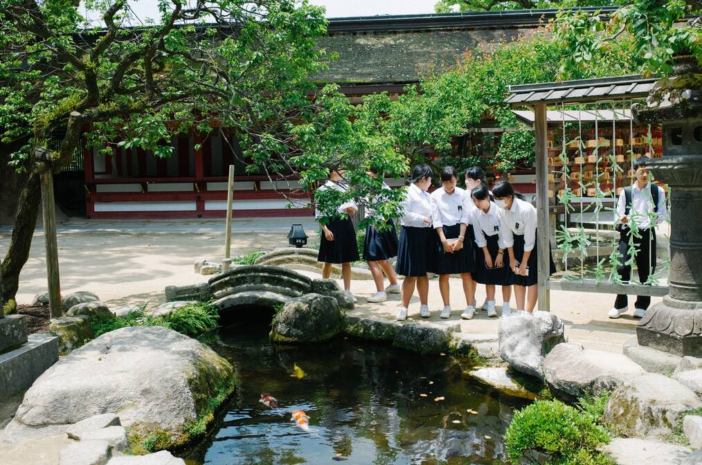 A group of students in uniforms stand around a koi pond.