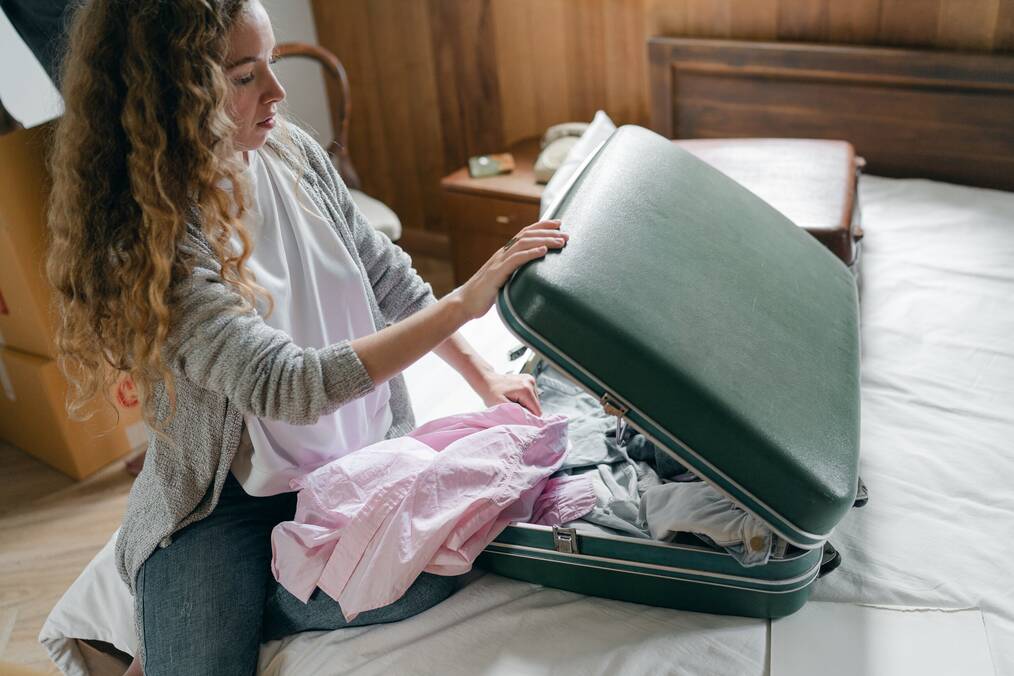 A young woman packs clothes in her suitcase on the bed
