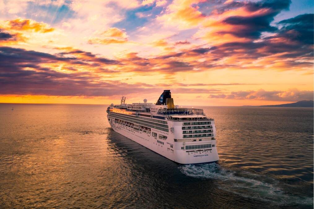 A cruise ship sails through the water at sunset.