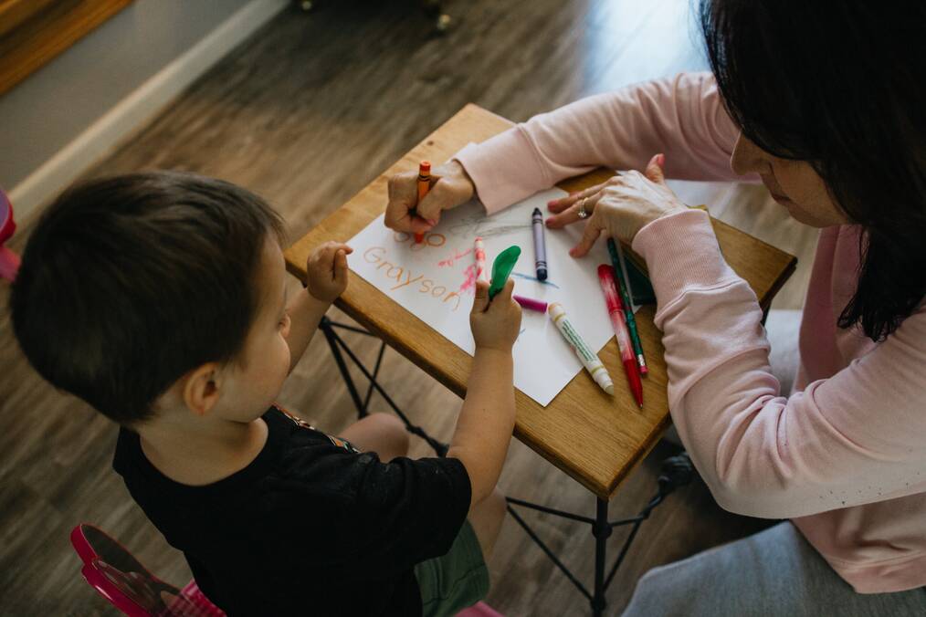 A woman colors on a small desk with a little boy.