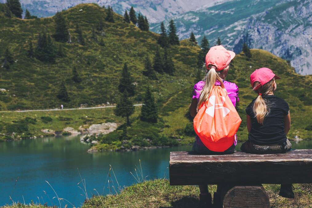 Two little girls sit with their backs to the camera in front of mountains.