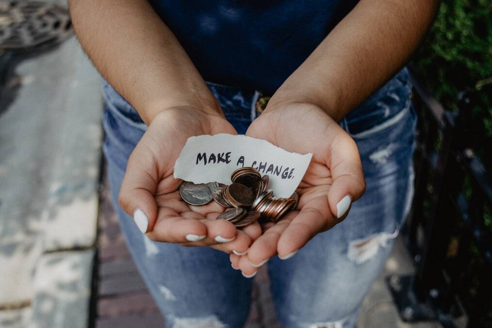 Hands hold coins and a note that says, "make a change".
