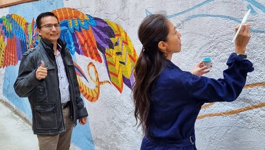 A man gives a thumbs up while a woman paints a wall.
