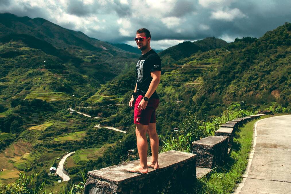 A man stands on a rock overlooking a green valley.
