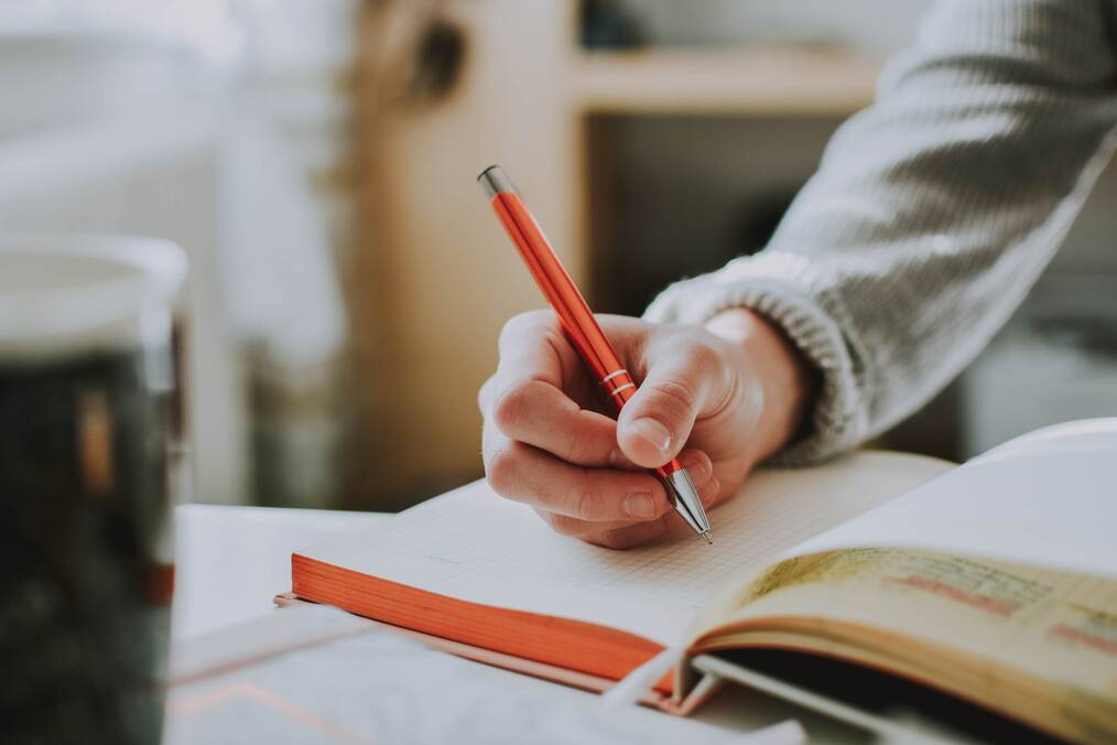 A hand holding a pen writes in a notebook.