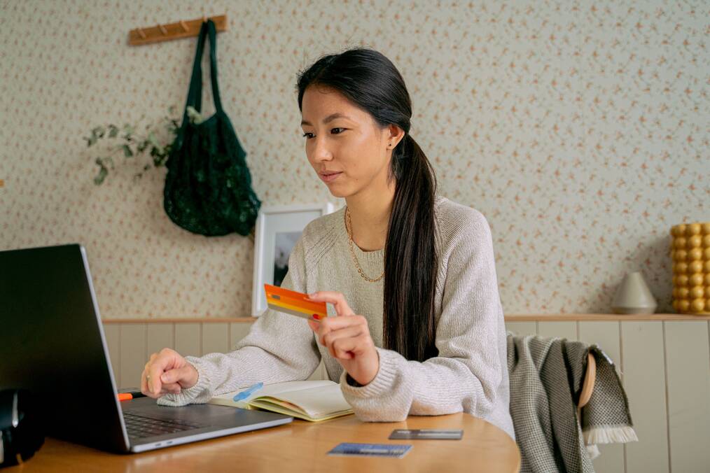 Person online shopping holding credit card in front of laptop