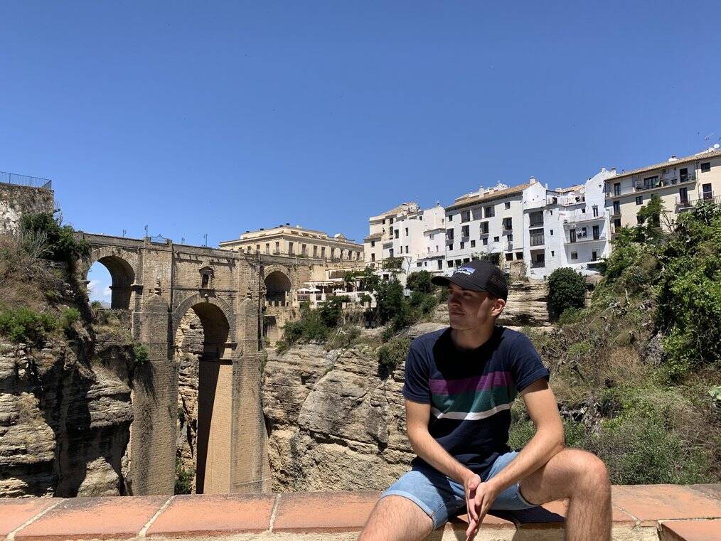 Man sits on wall with bridge in the background.