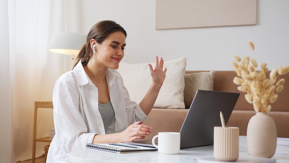 Cheerful woman waving and looking at laptop