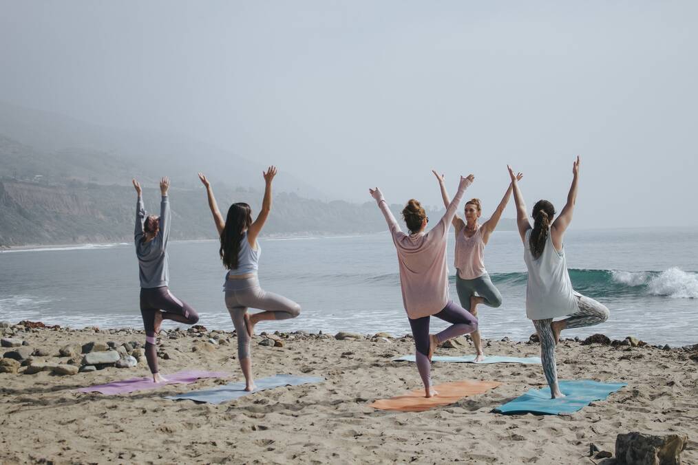 Women do yoga on a beach.