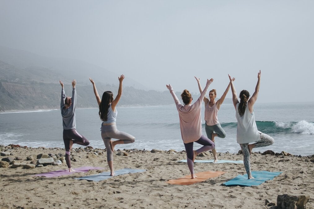 Photo by Kaylee Garrett on Unsplash Women do yoga on a beach.