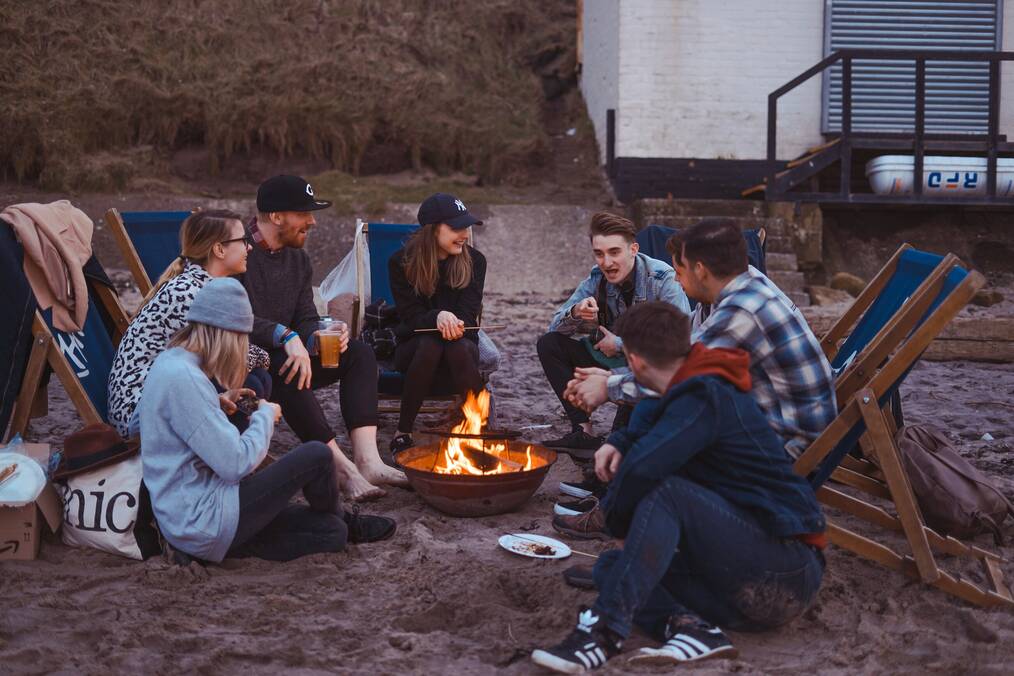 People sit around a campfire on a beach.