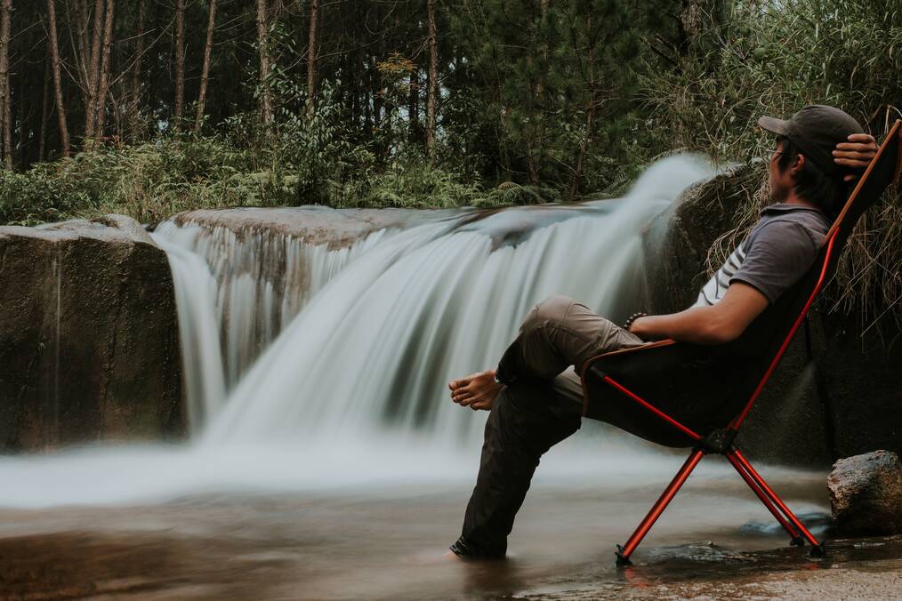 A man sits in a chair near a waterfall.