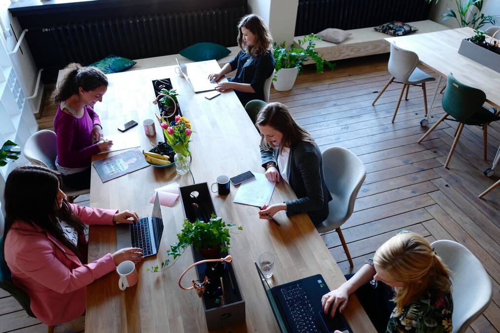 Women sit at a table working on laptops.