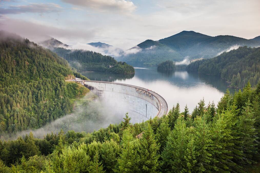 Bridge over a lake connecting forested mountains, under a layer of fog