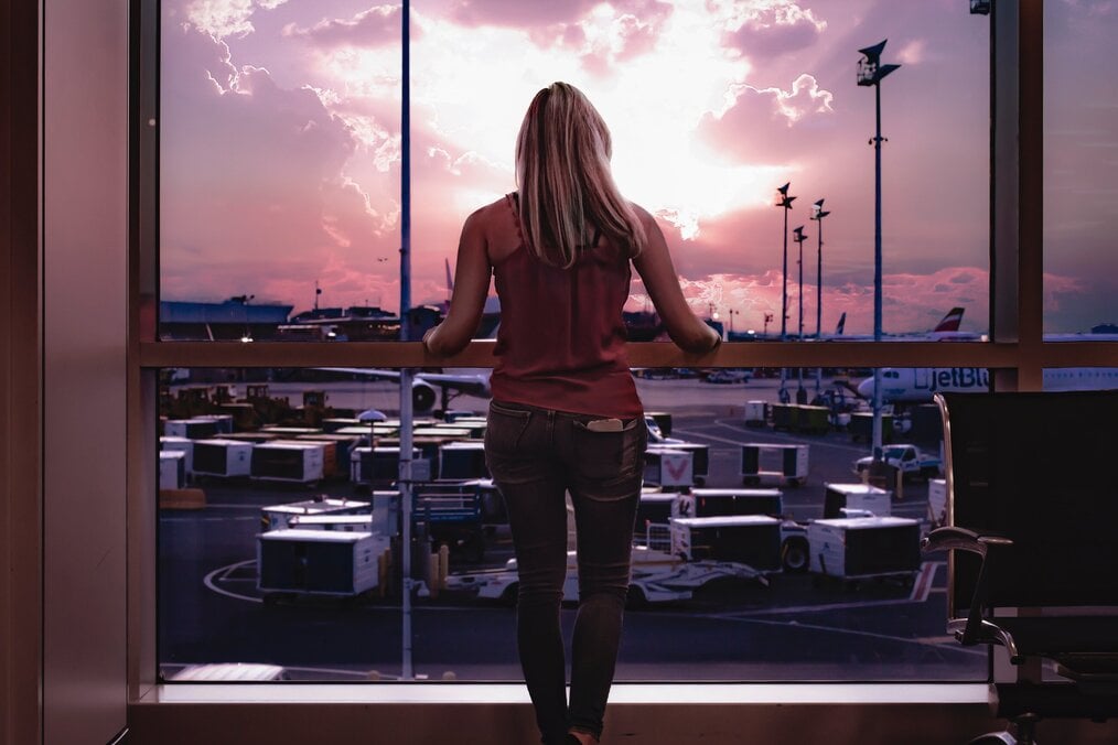 A woman stands in front of a window looking at a tarmac.