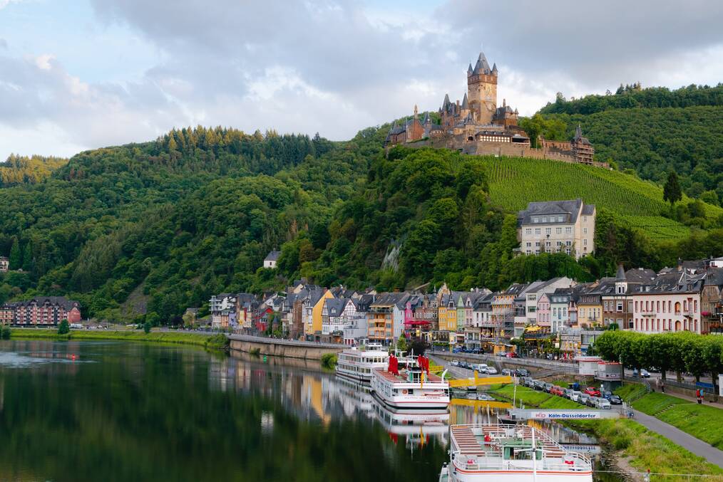A castle on a hill overlooks boats docked along a shore.