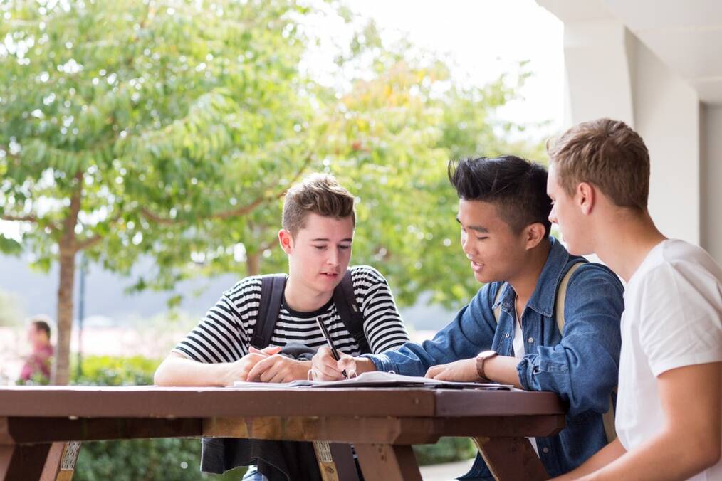Three young men sit outside at a picnic table studying.