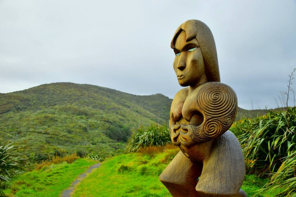 A Maori sculpture stands near a green hill.