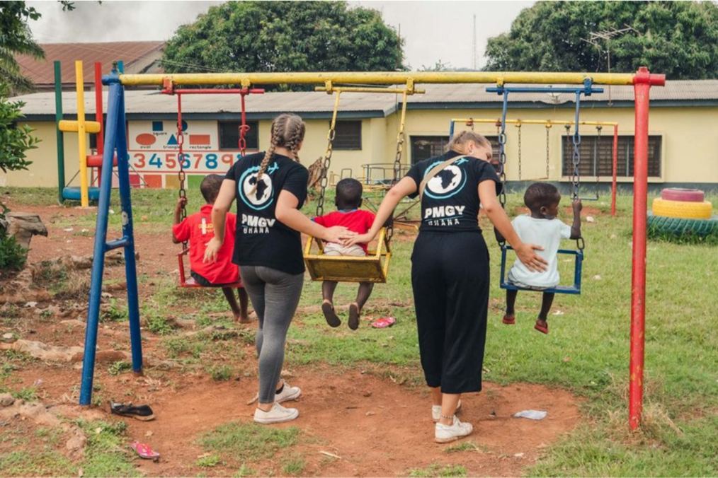 Two volunteers pushing children on a swing
