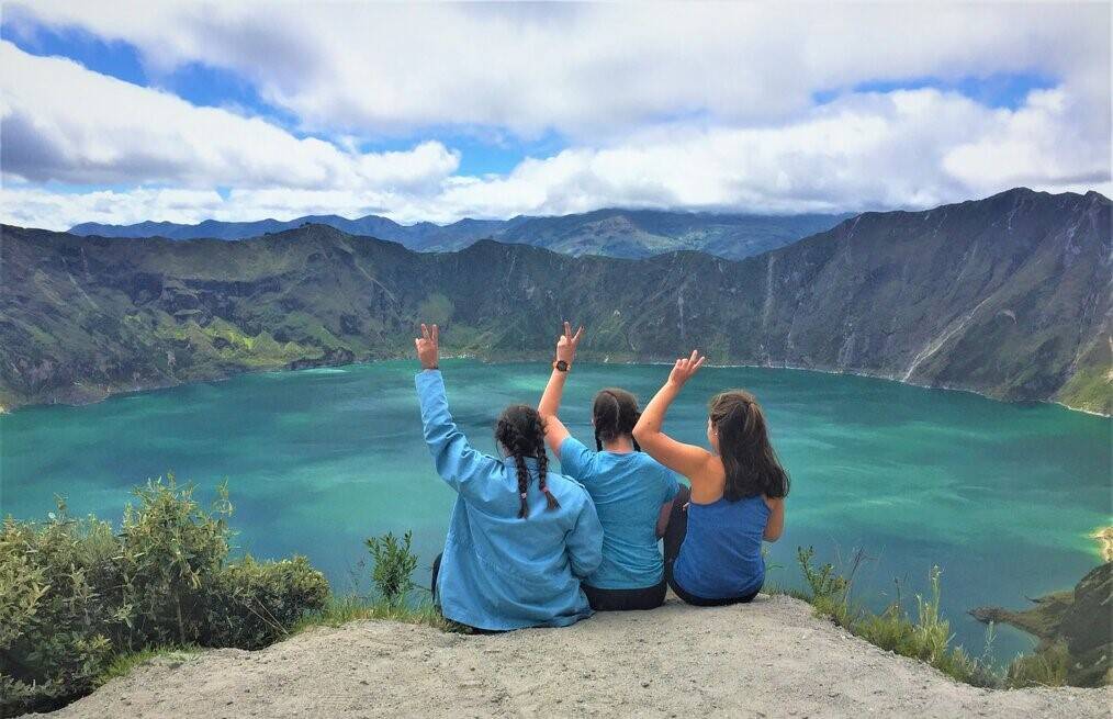 Three girls doing peace sign overlooking mountain and lake.