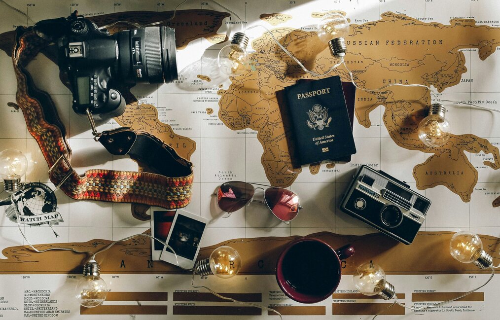 Photo by Charlotte Noelle on Unsplash A table covered with a map, photos, a passport, and a camera.