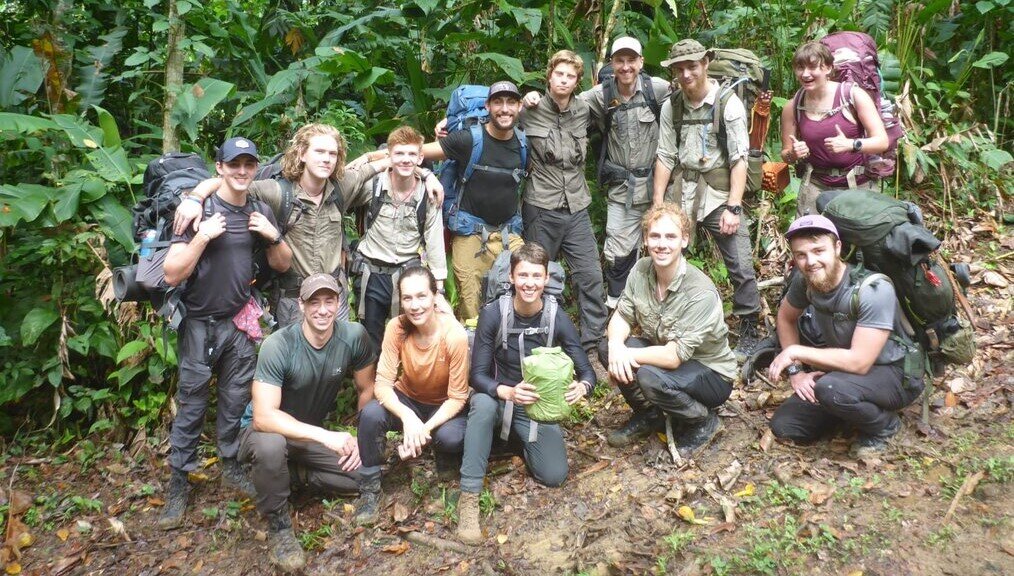 Gapforce A group with backpacks stands and smiles in the forest.