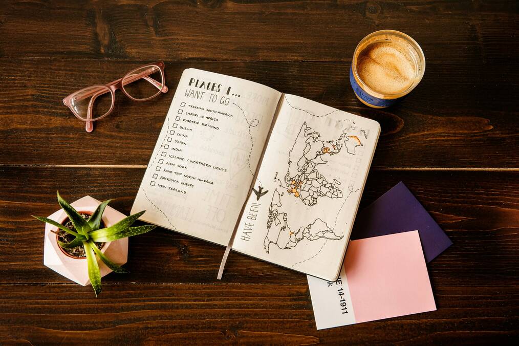 A notebook is open on a table with a cup of coffee beside it.