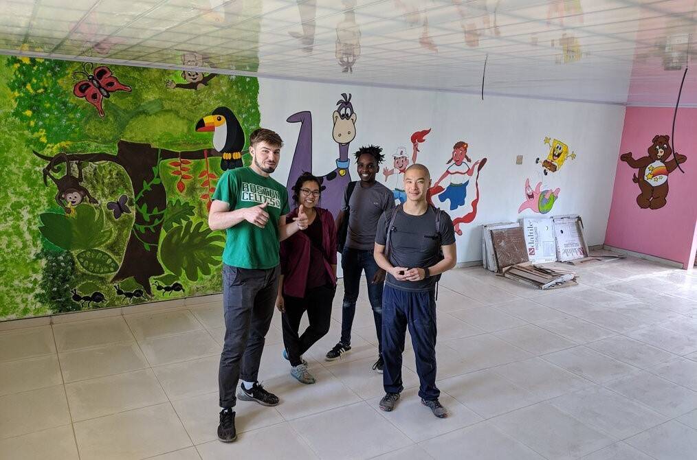 A group of people stand in front of a colorful mural and smile.
