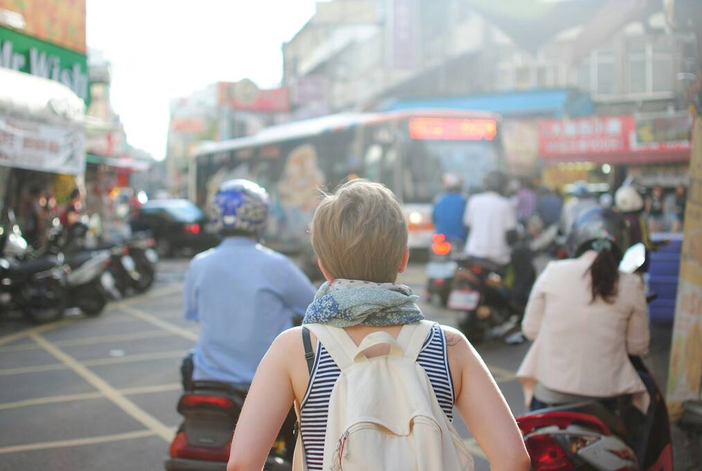 A woman faces away from the camera on a busy road.
