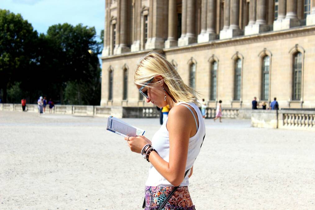 A woman standing near a building looks at a brochure.