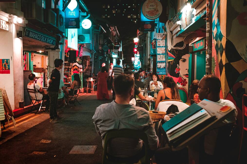 People sit outside on a street at night.