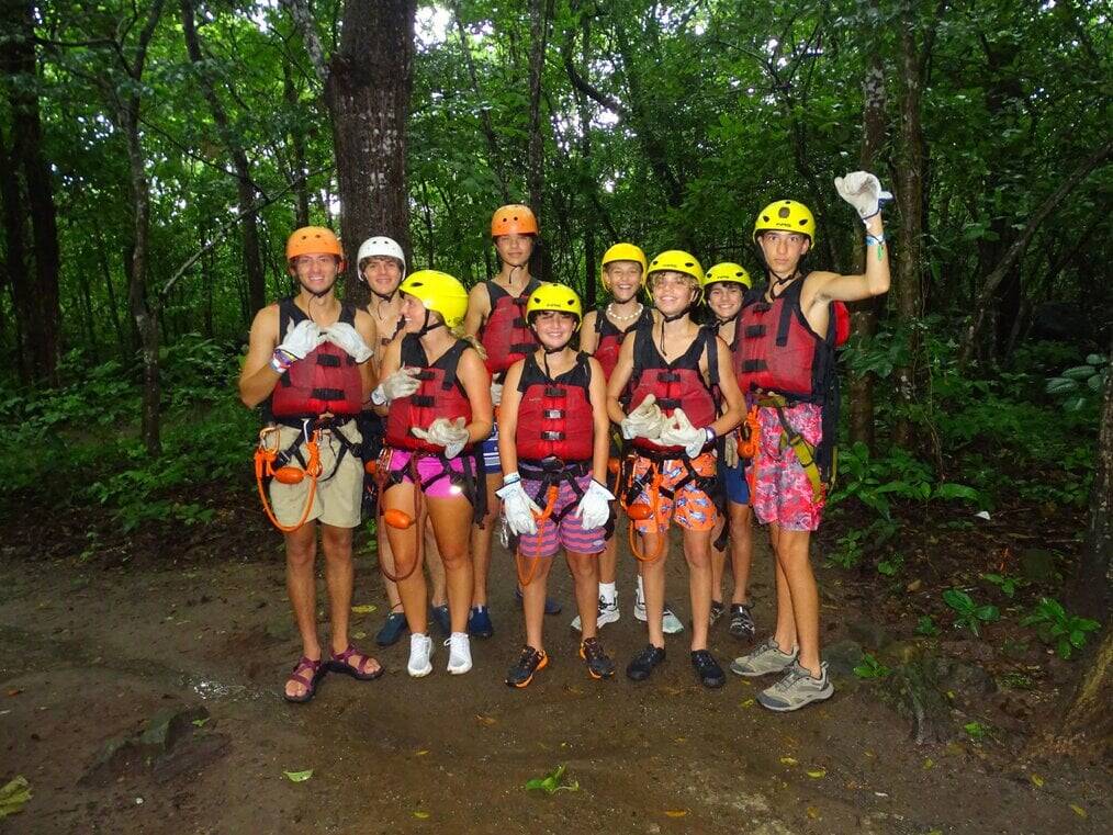 A group of teans wearing helmets and protective vests stand in the jungle.