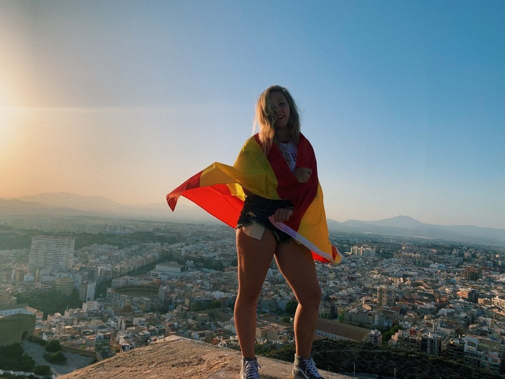 CIEE navigator A girl stands on a ledge with a Spanish flag draped around her shoulders.