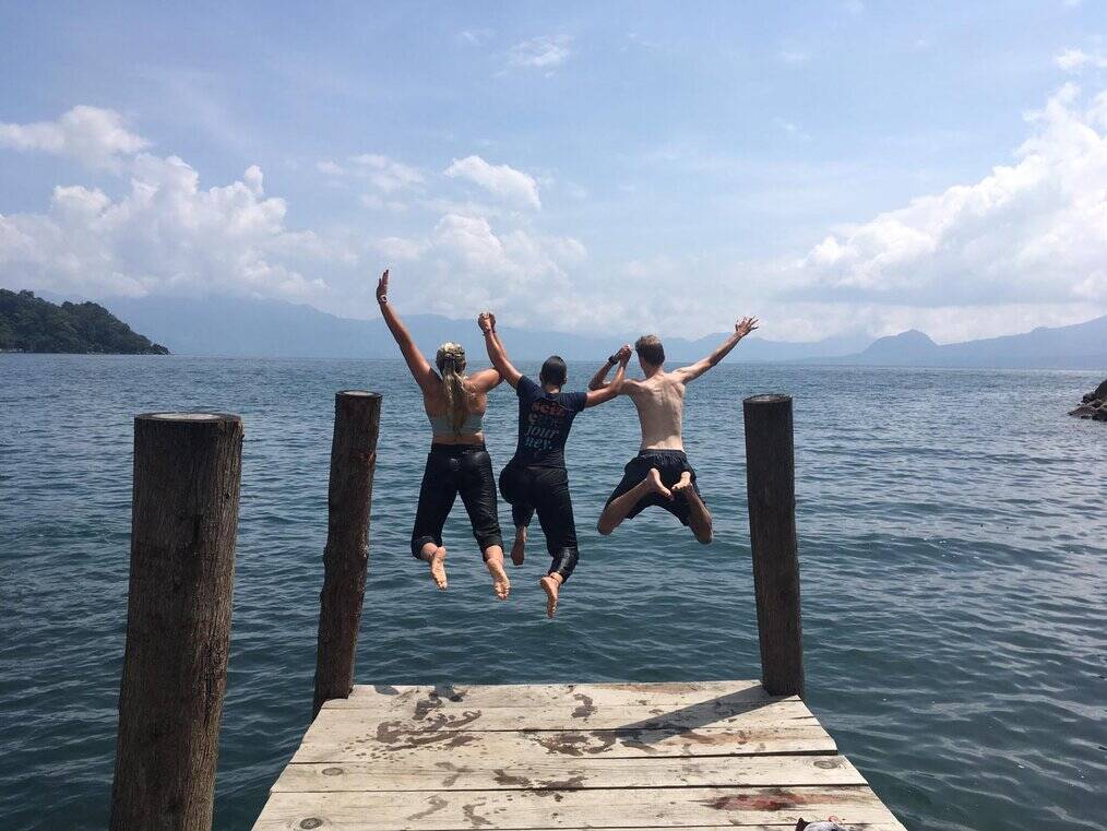 Three tens jump in the air at the end of a dock.