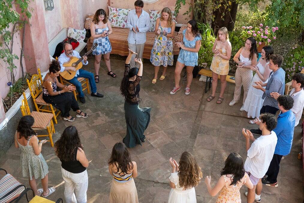 A group of teens stand in a circle around a woman flamenco dancing.