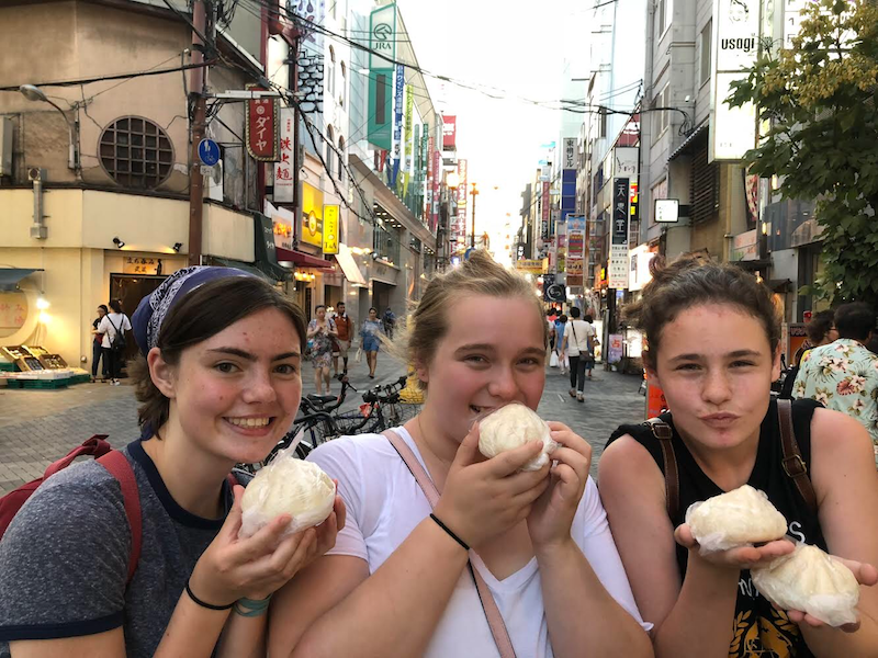 Three girls hold steamed buns in Japan.