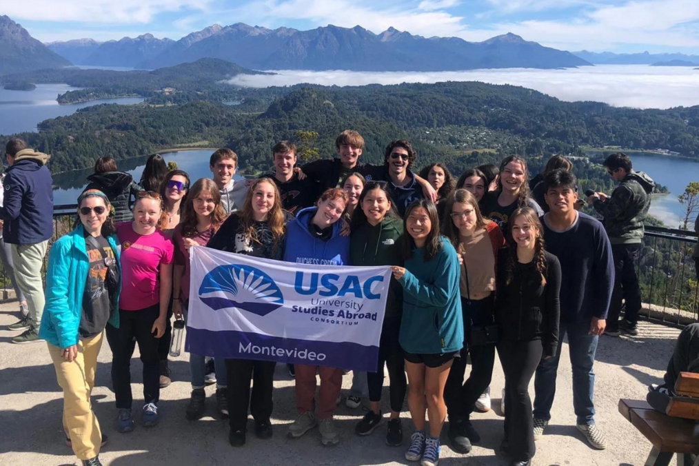 Study abroad students standing at mountain top holding banner