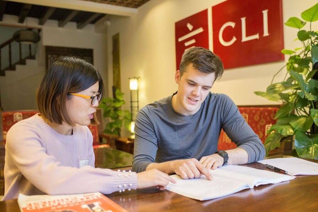 A man sits with his teacher and points at a book.